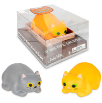 Introducing the Purrrly Kitty Cat in a Box by Archie McPhee: a set of two adorable stress squeeze squish toys, featuring one grey and one orange cat, each with enchanting green eyes. The orange cat comes packaged in a clear box decorated with the fun phrase "If she fits, she sits!" Ideal for stress relief for ages 3 and up.