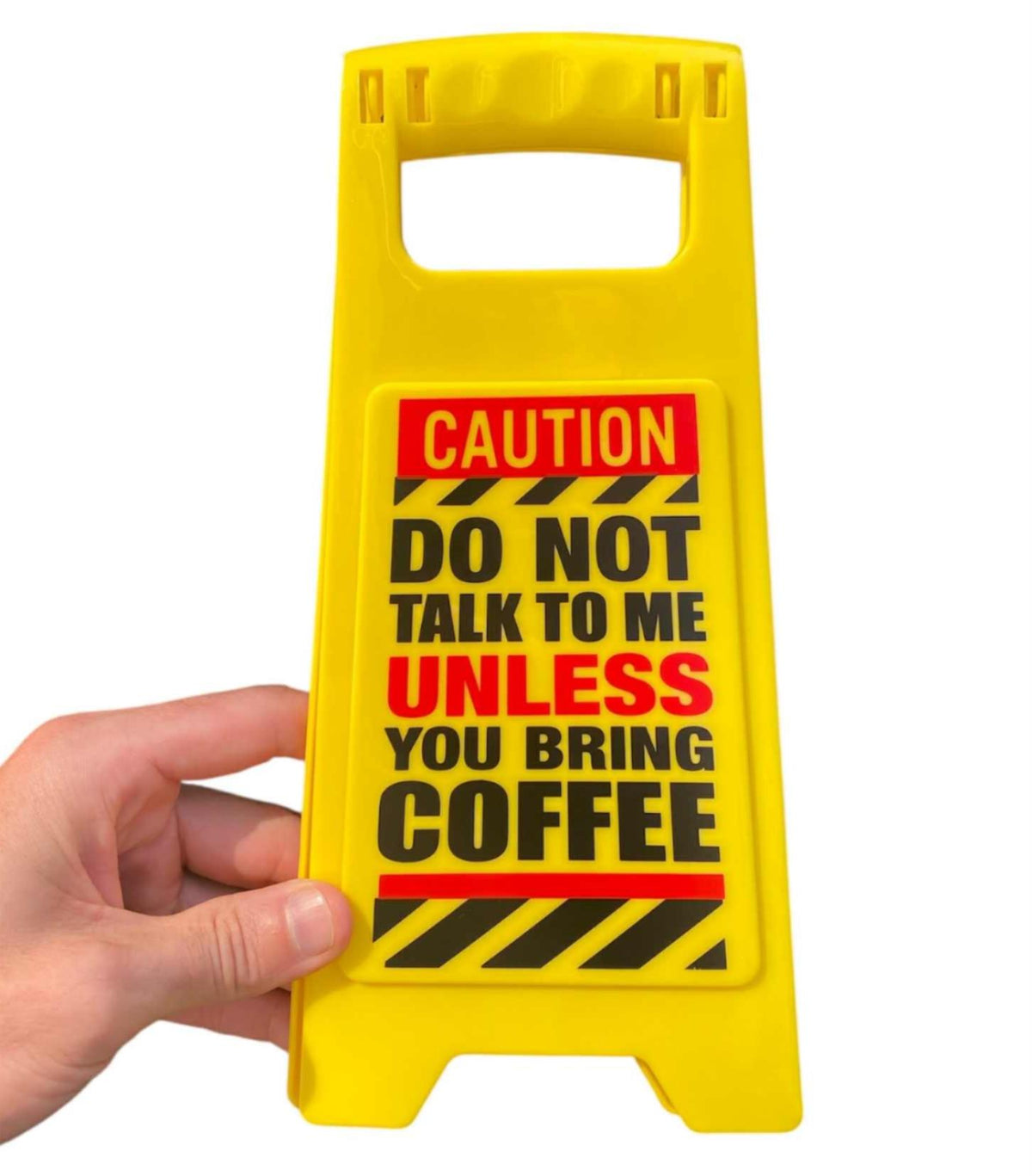 A hand holds the ⚠️ Funny Warning Bring Coffee Desk Sign ☕️, which reads: "CAUTION DO NOT TALK TO ME UNLESS YOU BRING COFFEE"—a hilarious office humor gag joke and perfect funny gift for your workspace.