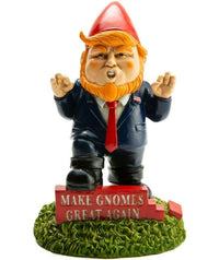 A quirky garden gnome, dressed in a red hat, blue suit, and red tie, stands on the grass beside a sign that reads "Make Gnomes Great Again." This amusing DONALD TRUMP GARDEN GNOME - Outdoor Home Yard Lawn Statue Sculpture from BigMouth is sure to brighten anyone’s day.