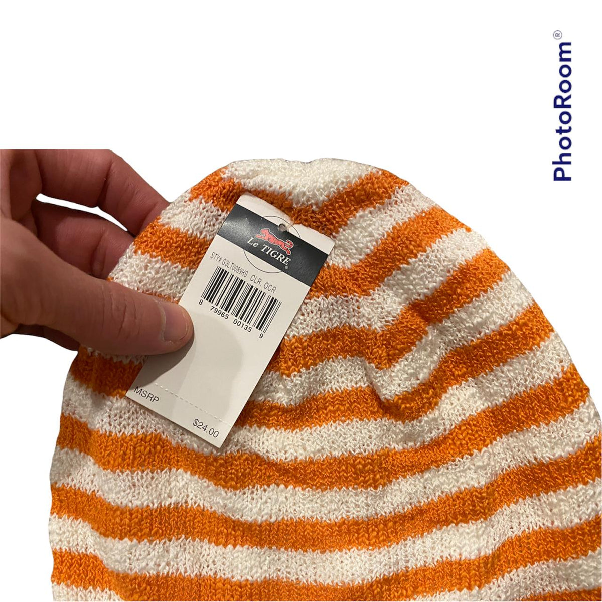 Close-up of a hand holding a Stylish Genuine Le Tigre Knit Hat Winter Beanie, featuring orange and white stripes, made from 100% acrylic, with a tag displaying a price of $34.00.