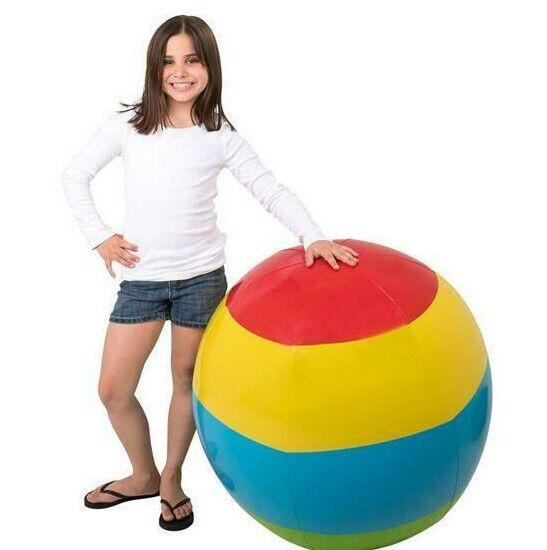 A girl in a white shirt and blue shorts stands next to the "Beach Ball HUGE 48" Inch Rainbow Inflatable 4 FT JUMBO Pool Luau Inflate Toy." She has one hand resting on the giant 4-foot beach ball and is smiling.