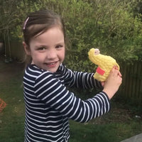 A young girl in a striped shirt is outdoors, smiling at the camera with greenery in the background, while holding the SPITTIN' LLAMA Water Pistol Squirt Gun - a funny child spray soaker kids toy.