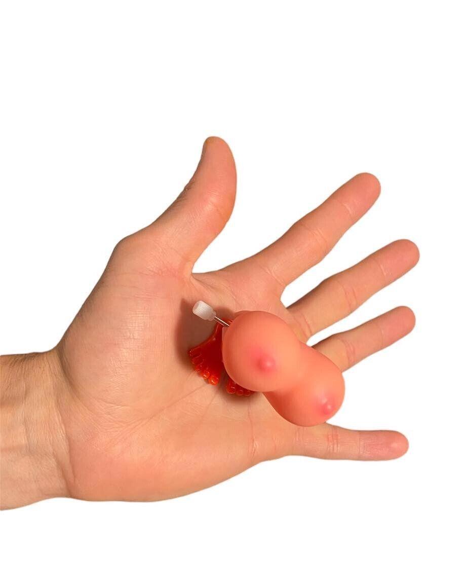 Hand holding a small, pink novelty item shaped like a pair of boobs from the "1 Jumping Boobie & 1 Pecker - Wind up Set - Funny Hen Party Novelty Adult Gift," against a white background, perfect as quirky decorations for adult parties.