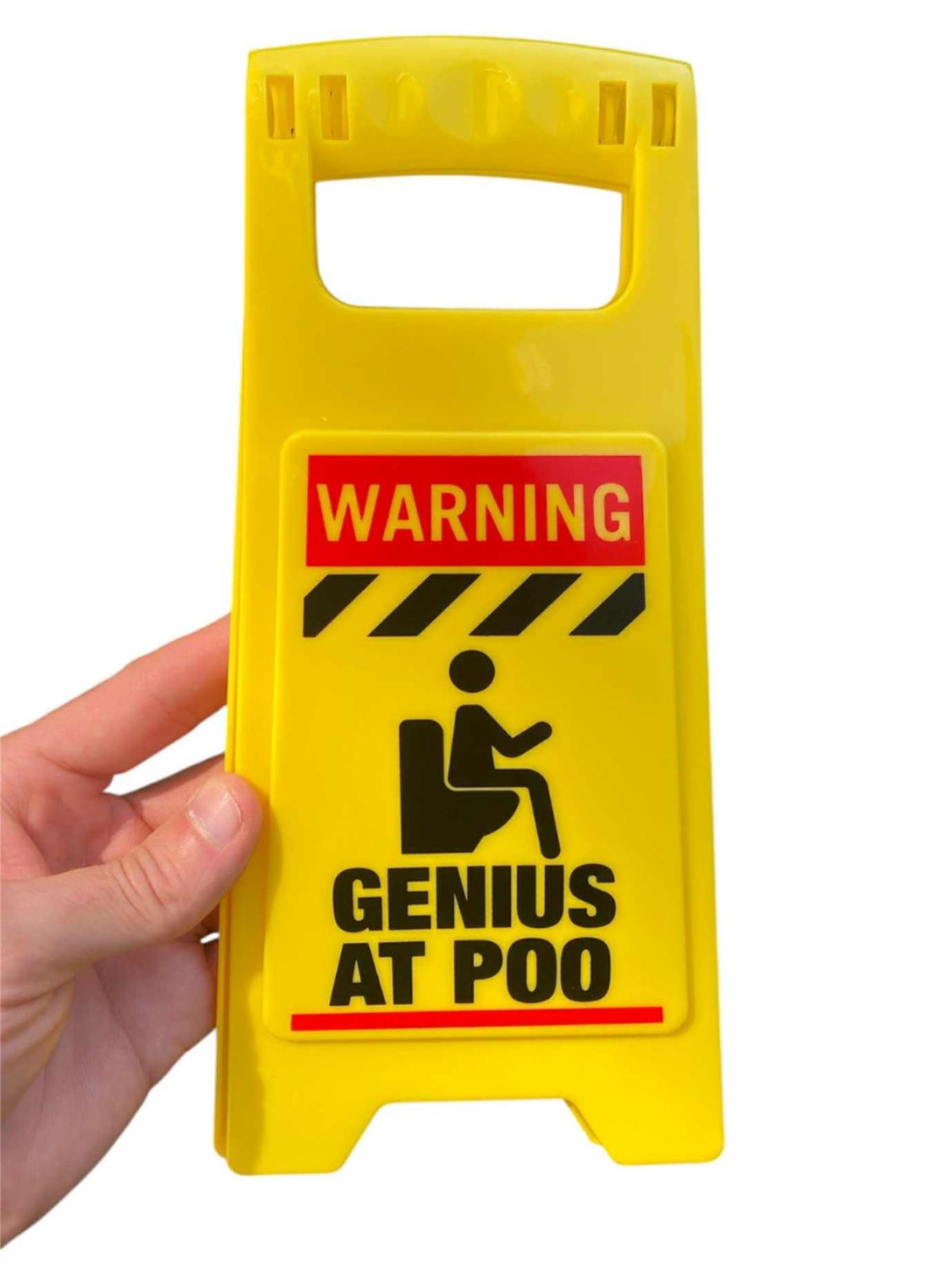 A hand holds the ⚠️ Funny Warning Genius Poo Desk Sign 💩 🚽, featuring "Warning: Genius at Poo" with a toilet illustration—ideal as an office humor gag or potty joke gift.