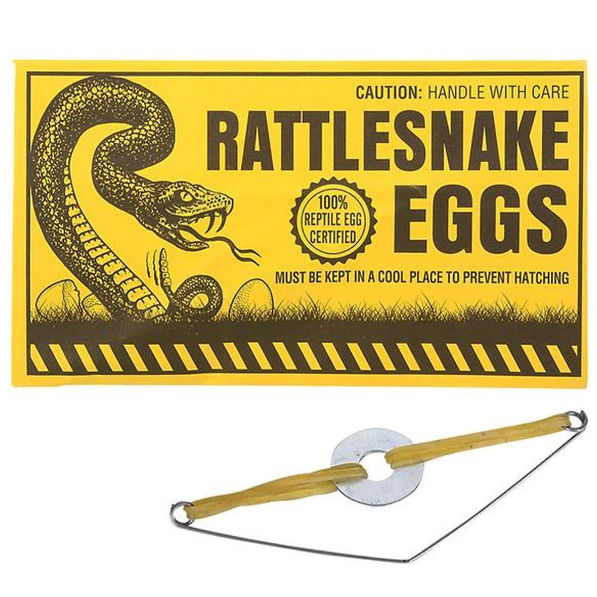 A yellow sign labeled "144 Prank Rattlesnake Egg Envelope - Novelty GaG Joke Gift Toy - Wholesale Lot" features a snake illustration and a caution note. Below it, a wire and rubber band prank device is placed, perfect for party favors or adding to your rattlesnake eggs prank collection.