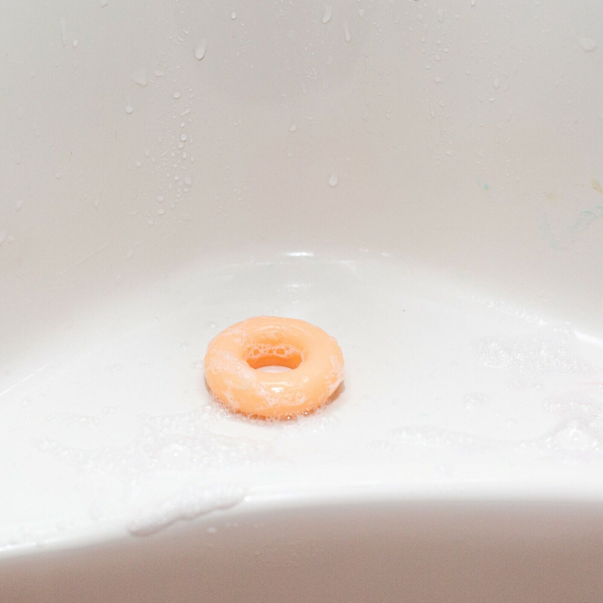 A peach-colored MINI MICRO ITTY-BITTY Willy Weener Soap from BigMouth rests on a wet, white surface, combining personal hygiene with a dash of humor—an ideal gag gift for any occasion.