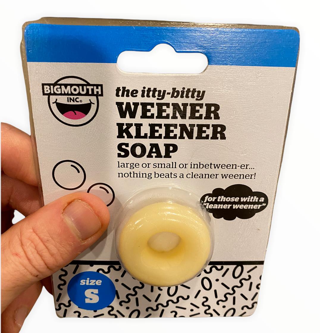 A hand holds "The MINI MICRO ITTY-BITTY Willy Weener Soap" by BigMouth, a ring-shaped soap designed for personal hygiene with the humorous tagline "For those with a cleaner weener!" Perfect as a gag gift, this size small product ensures cleanliness while providing a laugh.