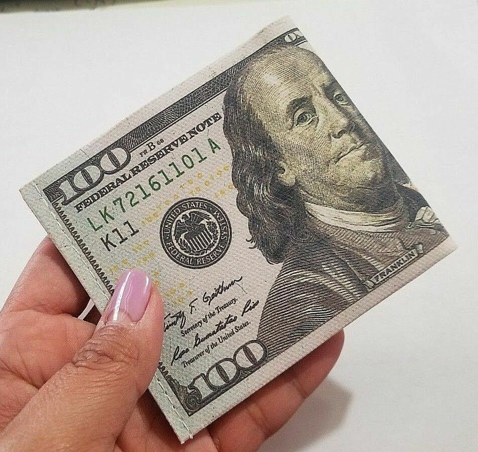 A hand with pink nail polish holds a folded $100 bill featuring Benjamin Franklin, fitting perfectly within the trendy 12 Pack - 100 Hundred Dollar Bill Wallets Money Bi-Fold Card Holder.