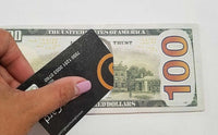 A hand with pink nails holds a black card with text, partially covering a $100 bill, making it a perfect snapshot for summer gifts like the 12 Pack - 100 Hundred Dollar Bill Wallets Money Bi-Fold Card Holder.