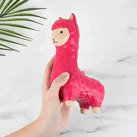 A hand holds a vibrant pink CALMA LLAMA Squishy Fidget Durable Squish—ideal as a stress-relieving pet toy gift—against a light background, with a green plant leaf partially visible in the top left corner.