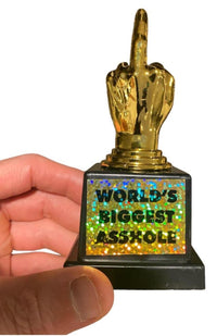 A person is holding a World's Biggest AS%HO#E Trophy Middle Finger F-U- Golden Award, featuring a gold hand with the middle finger raised. The trophy's base has a holographic label that reads "WORLD'S BIGGEST ASSHOLE," making it the perfect joke gag gift.