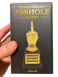 A hand holds a box labeled "World's Biggest AS%HO#E Trophy Middle Finger F-U- Golden Award." The box displays a humorous trophy shaped like a hand giving the middle finger, with the text "World's Biggest AS%HO#E" on its base. This joke gag gift is perfect for those who appreciate a touch of humor.