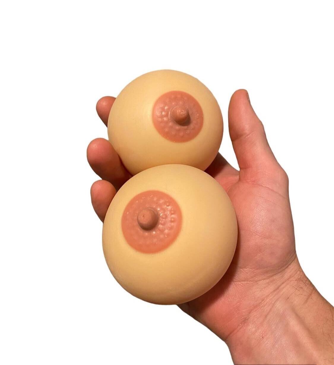 A hand displaying the 2pk Stress Boobs - Squeeze Boobies Feels Real! Adult Novelty Breast Man Toy Gift, ideal as a humorous present for those with a playful side. Whether refining your juggling skills or easing stress, these stress balls provide a cheeky take on relaxation.