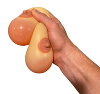 On a white background, a hand squeezes two silicone stress balls cleverly named "2pk Stress Boobs - Squeeze Boobies Feels Real! Adult Novelty Breast Man Toy Gift," complete with visible nipples. They are perfect for refining your juggling skills or offering as an amusing gag gift.