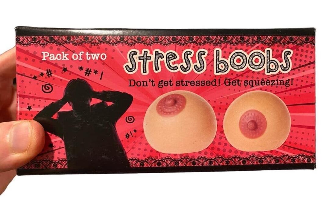 Box labeled "2pk Stress Boobs - Squeeze Boobies Feels Real! Adult Novelty Breast Man Toy Gift" containing two stress balls shaped like breasts. Text reads: "Don't get stressed! Master your juggling technique and start squeezing!" Ideal as a gag gift to bring laughter and relaxation.