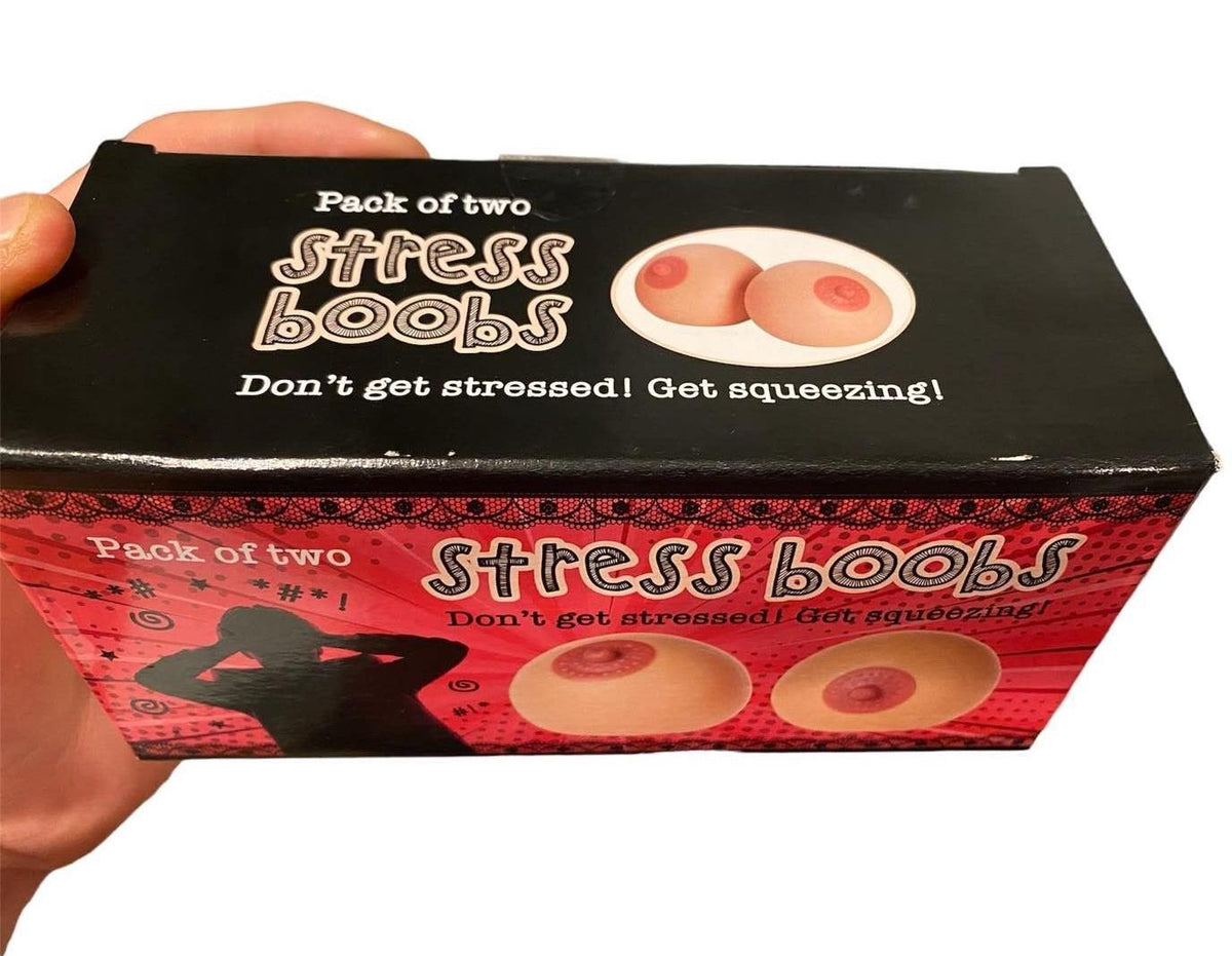 The image shows a hand holding a box labeled "2pk Stress Boobs - Squeeze Boobies Feels Real! Adult Novelty Breast Man Toy Gift," featuring stress balls shaped like breasts, ideal as a humorous gift. The packaging encourages, "Don't get stressed! Get squeezing!"—a playful reminder of balancing life's challenges.