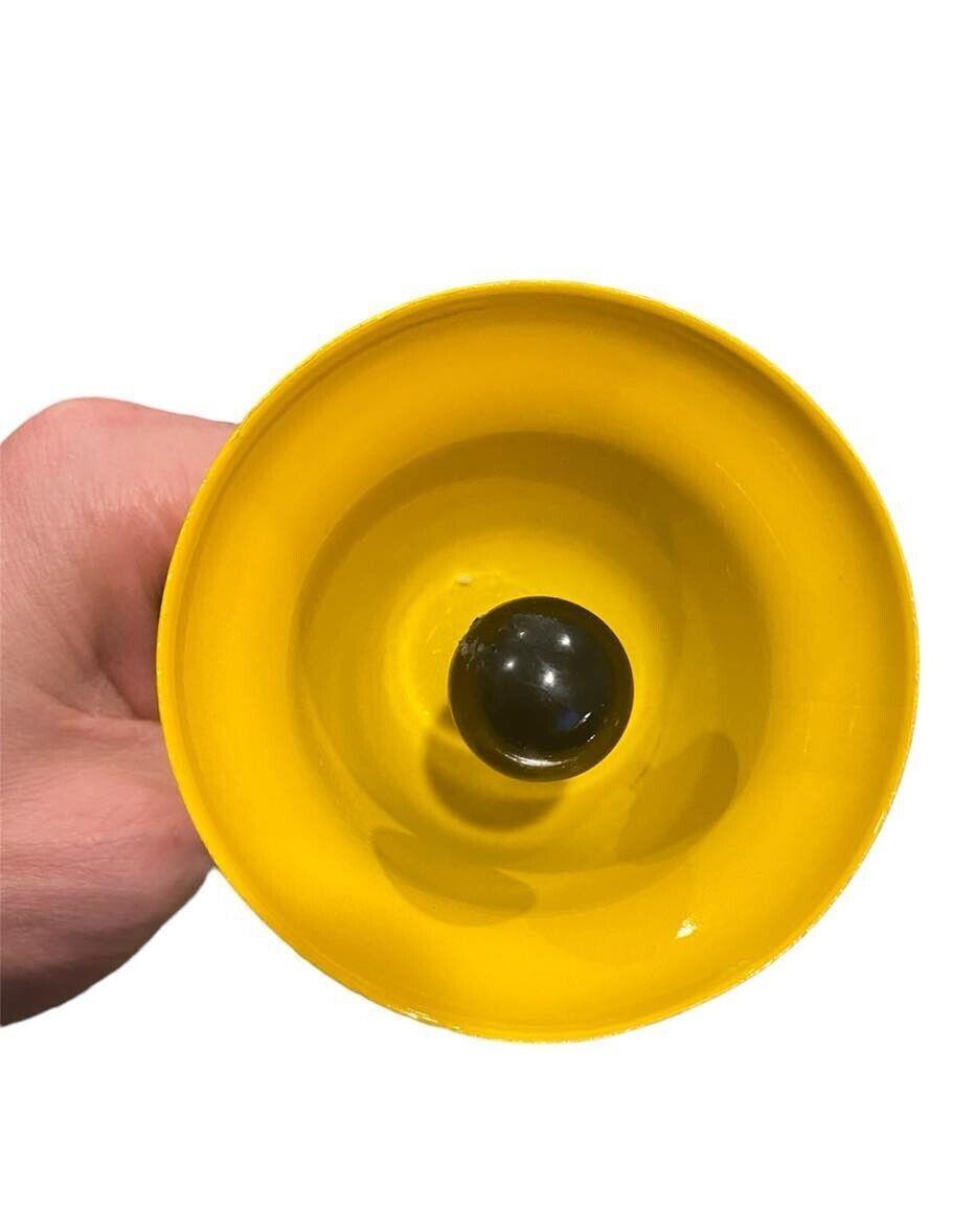 Close-up of a yellow funnel held by a hand, viewed from above with a black ball positioned in the center of the funnel opening. This quirky setup could easily be part of The FART ALERT Hand Bell—a great gift idea for pranksters!