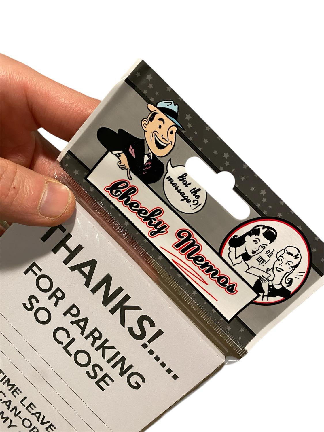 A hand holds a pack of "50-PK Cheeky Memo Note Pad – Thanks For Parking So Close! - Arseholes!" — an ideal notepad for humorously addressing parking etiquette, complete with a playful cartoon character as a clever gag gift.