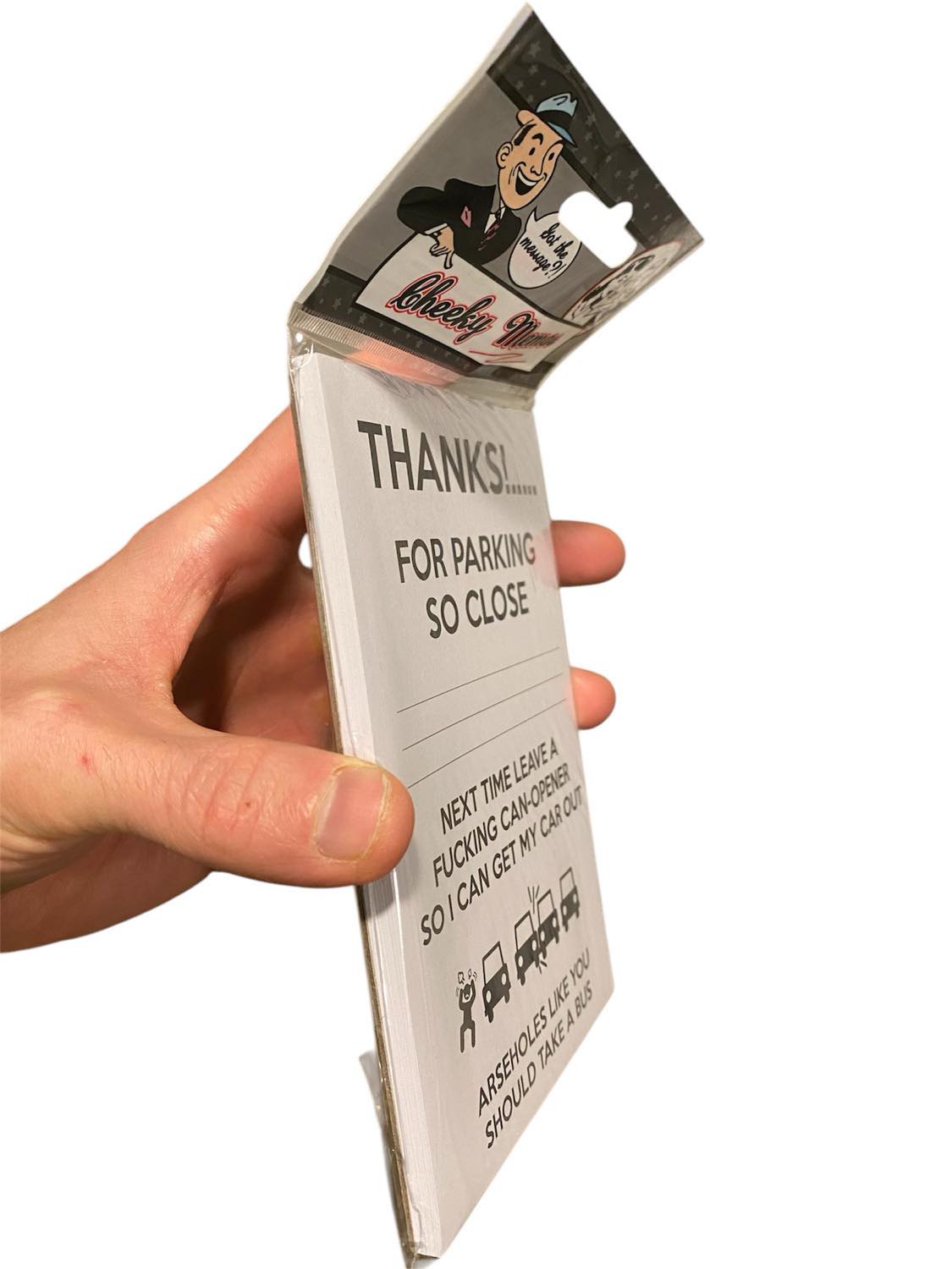 A hand holds a packaged 50-PK Cheeky Memo Note Pad, humorously titled "Thanks For Parking So Close! - Arseholes!"—making it the perfect gag gift.