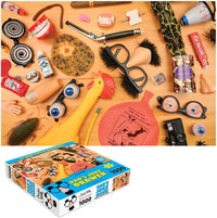 Beside the 1000-piece Dad's Joke Drawer Puzzle, themed around the quirky "Dad Jokes" from the Weird World of Archie McPhee, a tabletop is filled to the brim with novelty items like fake glasses, a rubber chicken, and a whoopee cushion, promising endless laughter for all.