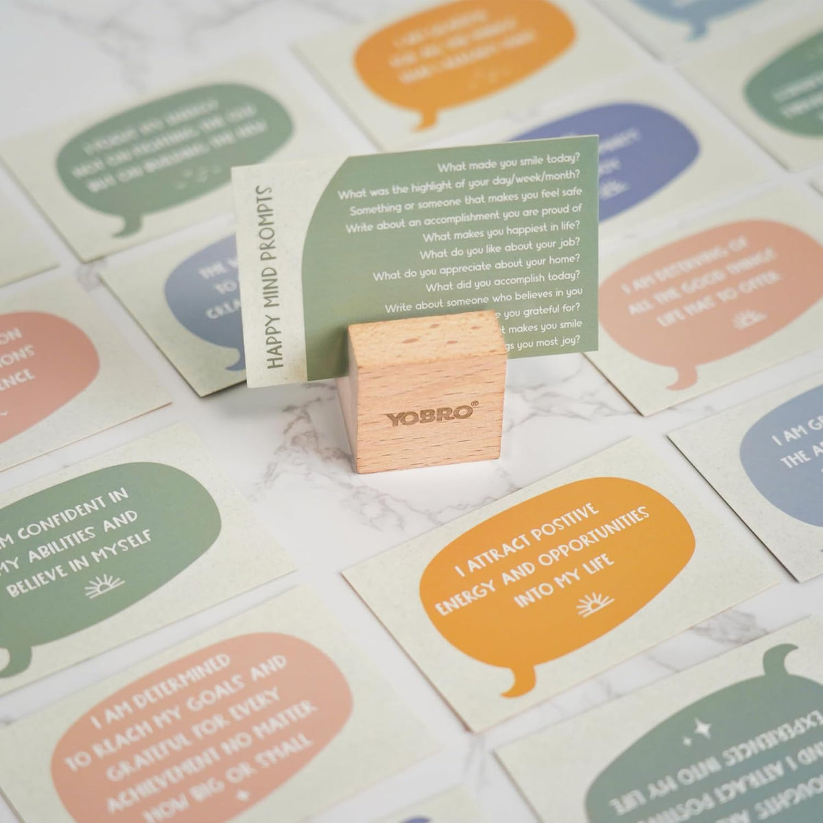 The 40 Positive Daily Quote Cards with Wooden Stand & Tin—motivational desk decor—features uplifting quotes on cards, held by a wooden stand, making a thoughtful self-care gift displayed on a light marble surface.