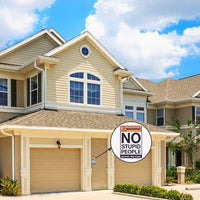 A large beige house showcases a unique decor item, a humorous metal tin sign located near the garage door that states, "Warning: NO STUPID PEOPLE Beyond This Point," which is the Metal Tin Sign Bar Man Cave #C-101.