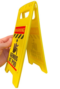 A hand holds the ⚠️ Funny Warning Genius Poo Desk Sign 💩 🚽—a hilarious office humor gag, perfect as a prank or desk gift for coworkers who love jokes!.