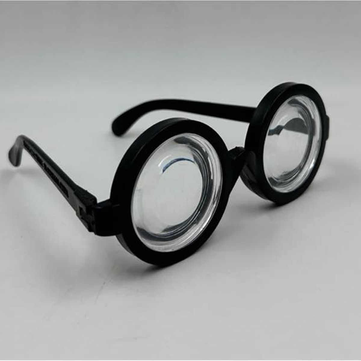 The Senior Citizens Old Magni-Vision - Over the Hill Magnify Eyes Glasses Gag Gift, featuring round, thick frames and clear lenses, rest elegantly on a flat surface, offering both style and practicality.