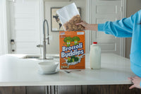Someone pours cereal from the 🥦 Prank Cereal Box – Broccoli Buddies Gag Gift Box | Funny Joke Prank Present🎁 into a bowl on a kitchen counter beside a spoon and milk.