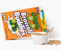 A 🥦 Prank Cereal Box – Broccoli Buddies Gag Gift Box🎁 lies on its side. Inside, the bag and cereal in the bowl are Cheerios, with some pieces scattered around.