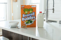 A 🥦 Prank Cereal Box – Broccoli Buddies Gag Gift Box | Funny Joke Prank Present🎁 sits with a bowl, spoon, and plastic milk jug on the kitchen counter near the sink.