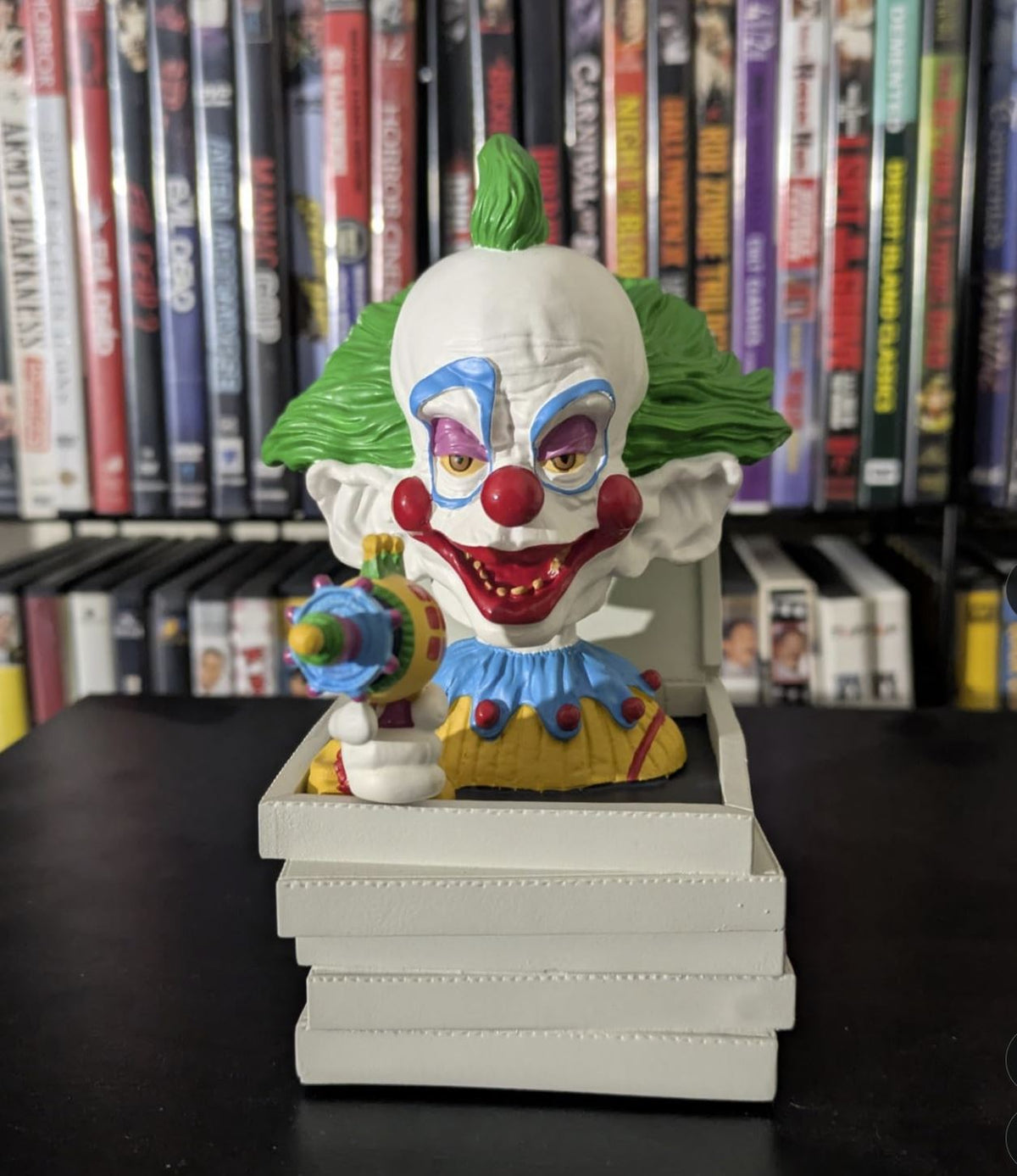 The Killer Klowns 🤡 Shorty in Pizza Box Bobblehead Statue Figure by Royal Bobbles features a sinister green-haired clown holding a toy ray gun, perfect for display in front of your DVD collection.