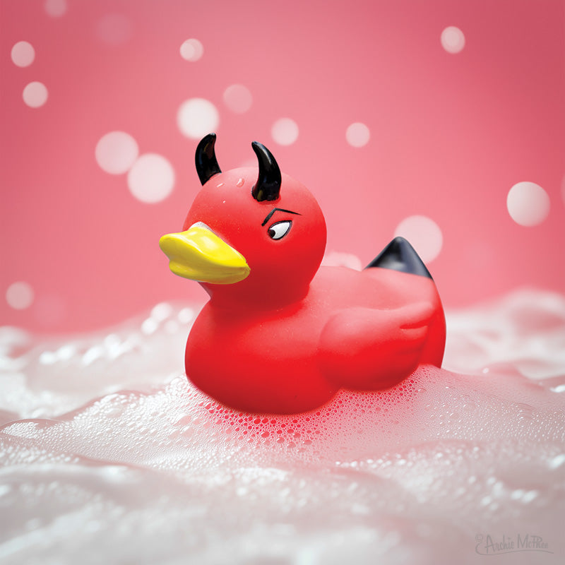 The 😈 Devil Duckie Rubber Bath Toy – a red floating demon duck with black horns and tail – floats in soapy bubbles with a pink background and white bokeh lights. Perfect as a funny gag gift!.