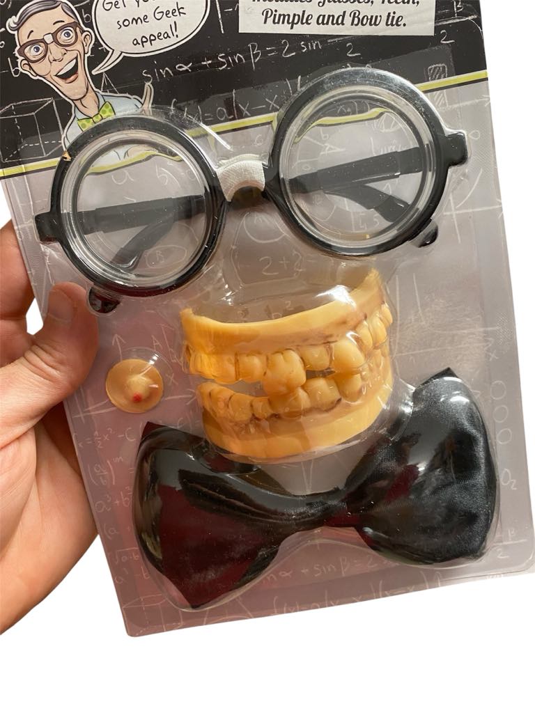 Instant Geek Costume Kit 🤓 includes glasses, oversized fake teeth, a black bow tie, and a yellow pimple button—perfect for nerd dress up or as a funny gag gift. Comes in packaging held by a hand.