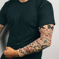 A person wears a black t-shirt and Christmas Holiday Tattoo Sleeves 2pk – Funny Fake Arm Tattoos Costume Party, featuring festive realistic designs, and stands against a plain background.