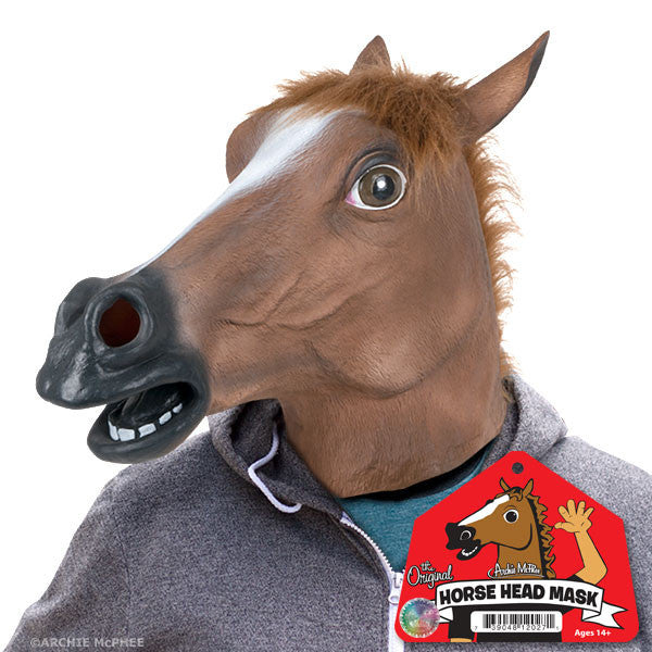 A person is wearing THE ORIGINAL HORSE MASK by Archie McPhee, featuring large eyes, a prominent snout, and an open mouth; the product's packaging is visible in the foreground.