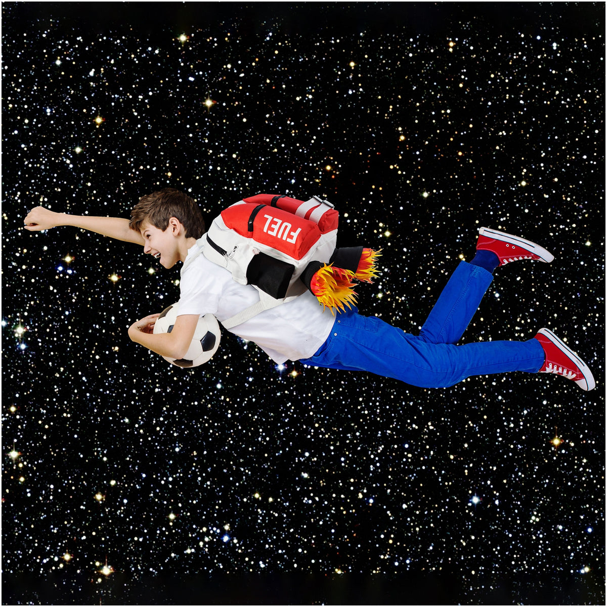 A boy with a Kids Jetpack Backpack Rocket School Bag appears to fly with a soccer ball through a starry space background, wearing blue pants and red sneakers.