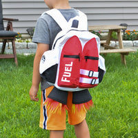 A child stands on grass in a backyard wearing the Kids Jetpack Backpack Rocket School Bag 🚀, designed like a jetpack with "FUEL" and flame details—perfect for space astronaut costumes or as a fun travel gift.