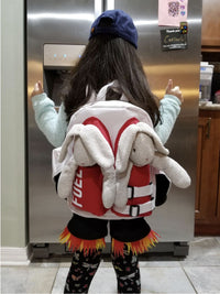 A child stands facing a refrigerator, giving thumbs up while wearing the Kids Jetpack Backpack Rocket School Bag 🚀, designed like a space astronaut jetpack and filled with plush bunnies and flame-decorated shorts.