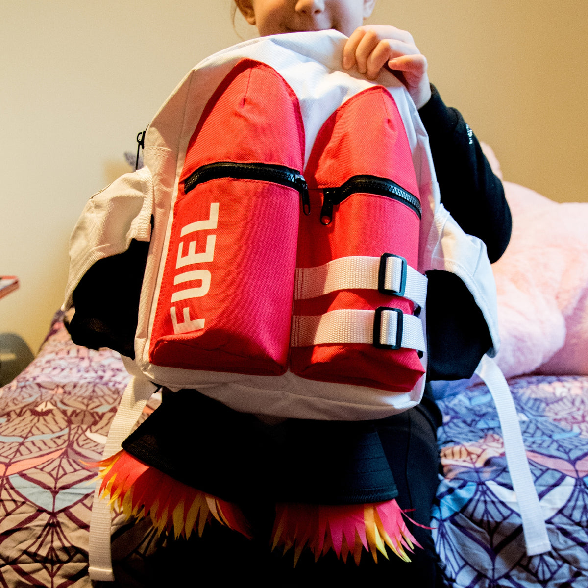 A person holds the Kids Jetpack Backpack Rocket School Bag, designed like a jetpack with red fuel tanks, white straps, and flame decorations—perfect for astronaut costumes or as a fun travel gift.