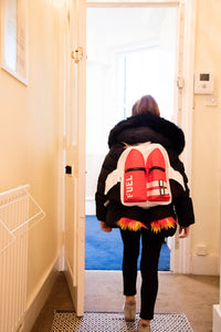 A person wearing a black coat and the Kids Jetpack Backpack Rocket School Bag 🚀 Space Astronaut Costume Travel Gift walks through a doorway into a brightly lit room.
