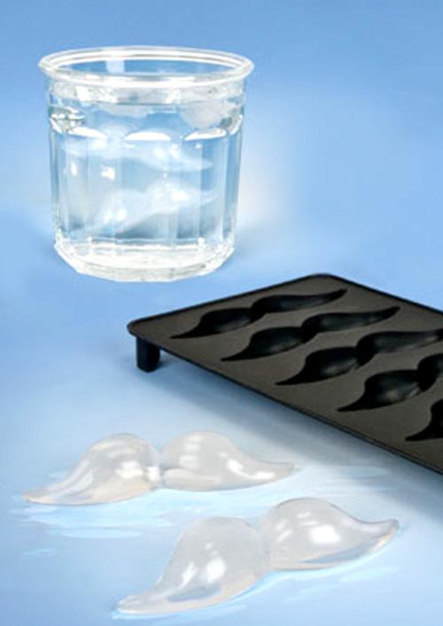 A glass of water with mustache-shaped ice cubes, courtesy of the Mustache Ice Cube Tray by Archie McPhee, sits next to the sleek black silicone mold on a blue background, creating the perfect vibe for a quirky mustache-themed party.