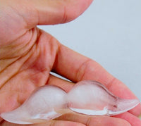 A hand holds a small, clear ice sculpture shaped like a mustache, crafted from the Mustache Ice Cube Tray by Archie McPhee, adding a playful touch to the festivities of a mustache party.