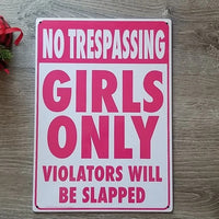 On a weathered wooden surface sits the Metal Tin Sign "No Trespassing: Girls Only Violators Will Be Slapped" #B-101.