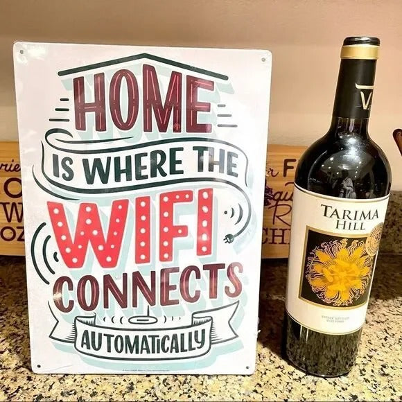 A bottle of wine is paired with the charming Metal Tin Sign "Home is Where the WiFi Connects Automatically" Wall Decor #H-101, adding a whimsical touch to your home decor and serving as a clever gift idea for friends.