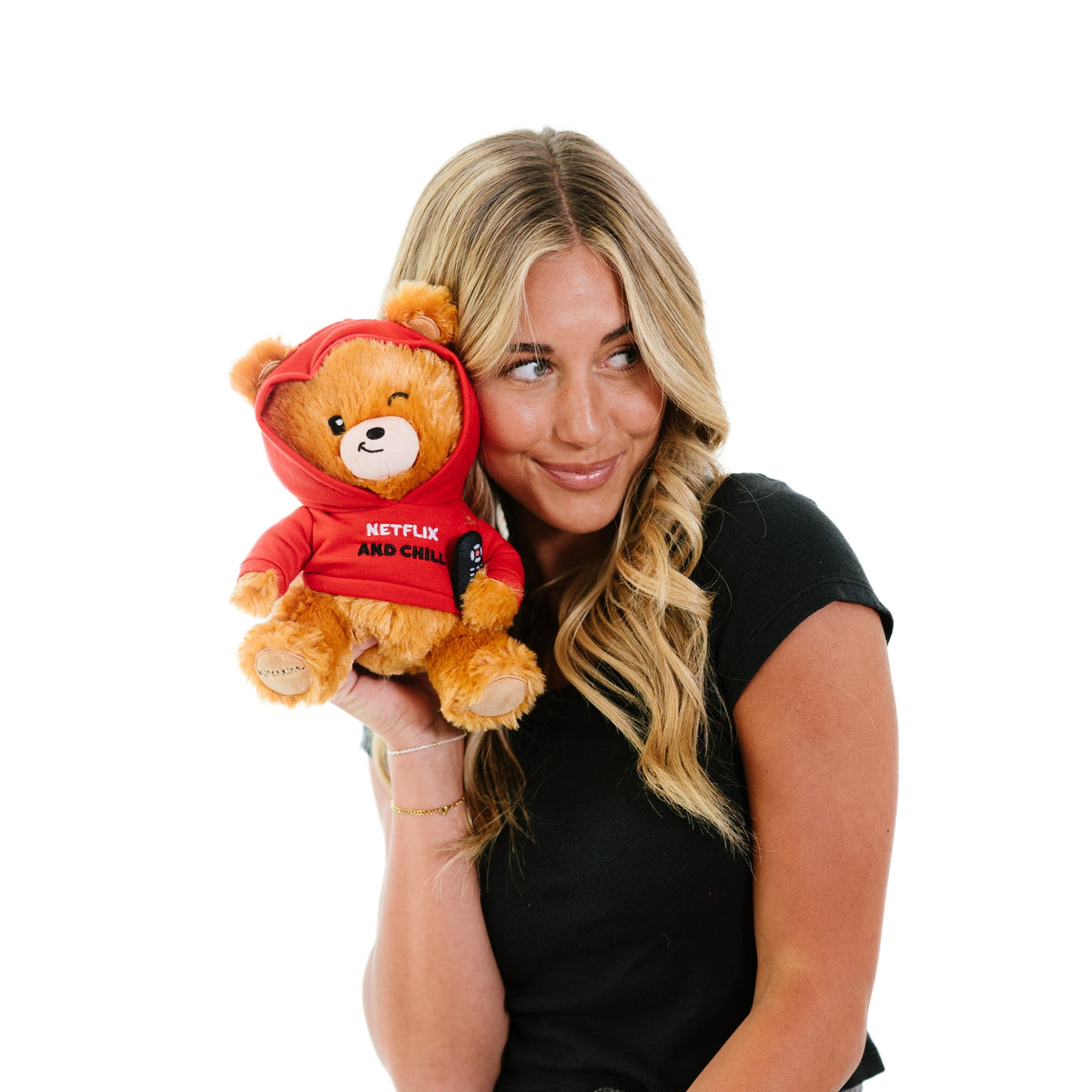 A woman with long blonde hair holds a Punchkins "Netflix & Chill" Teddy Bear Plushie—a cuddly gift for movie fans—in a red hoodie, against a white background.