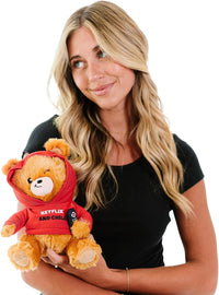 A woman with long blonde hair in a black t-shirt holds the Punchkins "Netflix & Chill" Teddy Bear Plushie, a cuddly movie fan’s gift in a red hoodie, against a white background.