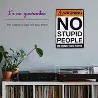 A room featuring a turntable, records, and a plant is accented by the Metal Tin Sign "Warning: NO STUPID PEOPLE Beyond This Point" Bar Man Cave #C-101, adding a touch of novelty decor.