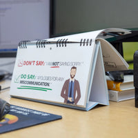 The "Professional Insults - Desk Spiral Flip Book - Funny Office Message Table Signs" features a page with the text, "DON'T SAY: 'I am NOT saying sorry.' DO SAY: 'Apologies for any miscommunication.'" This HR-approved resource comes with a graphic of a man and provides a tactful guide for handling workplace comebacks professionally.