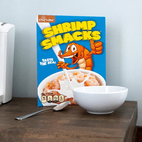 The 🦐 Prank Cereal Box – Shrimp Smacks Gag Gift Box sits by a white bowl and spoon, featuring a cartoon shrimp and the slogan "Taste the sea!"—a hilarious, funny joke present for any prankster.